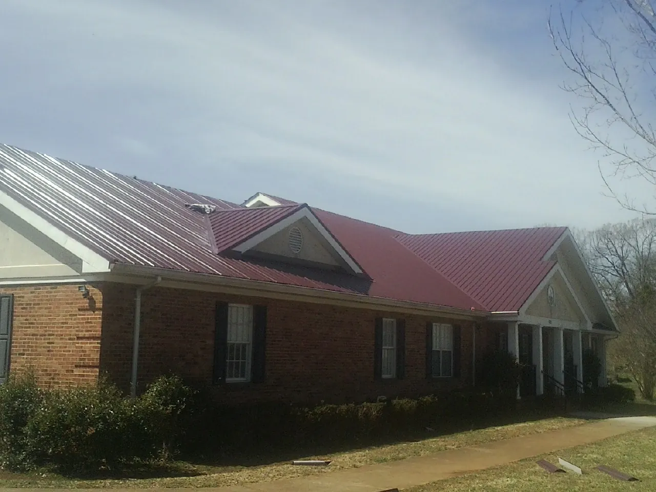 Red metal roof with gabled entries on a long brick building, from a Hail Damage Roof Repair job in Green Camp