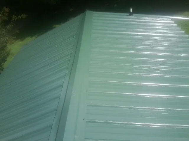 New green metal panels meeting at the ridge of a roof — Flat Roof Repair work by our crew in Green Camp