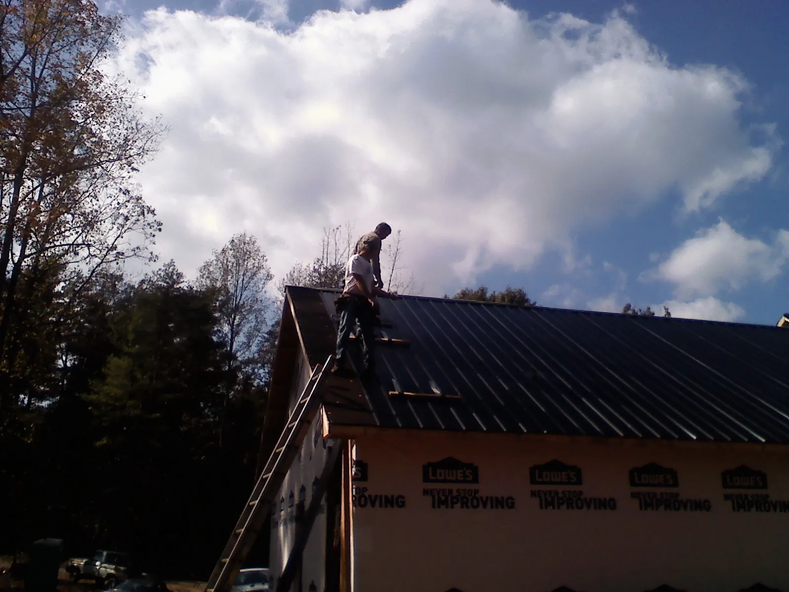 Roofer fastening dark metal panels high against a cloudy sky, from a Roof Inspection job in Green Camp