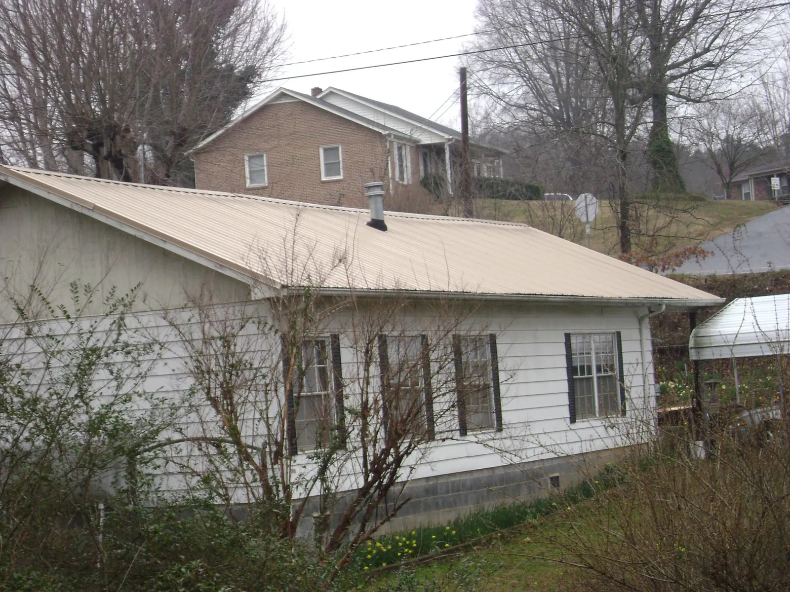 Tan metal roof on a white sided house set into a hillside — Commercial Roofing by Roofing Brothers in Green Camp