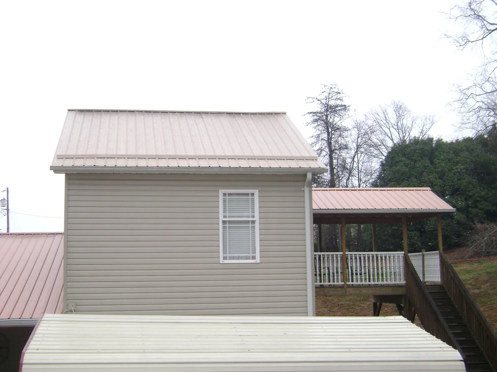Tan metal roofs on a two story addition and attached porch, from a Roof Replacement job in Green Camp
